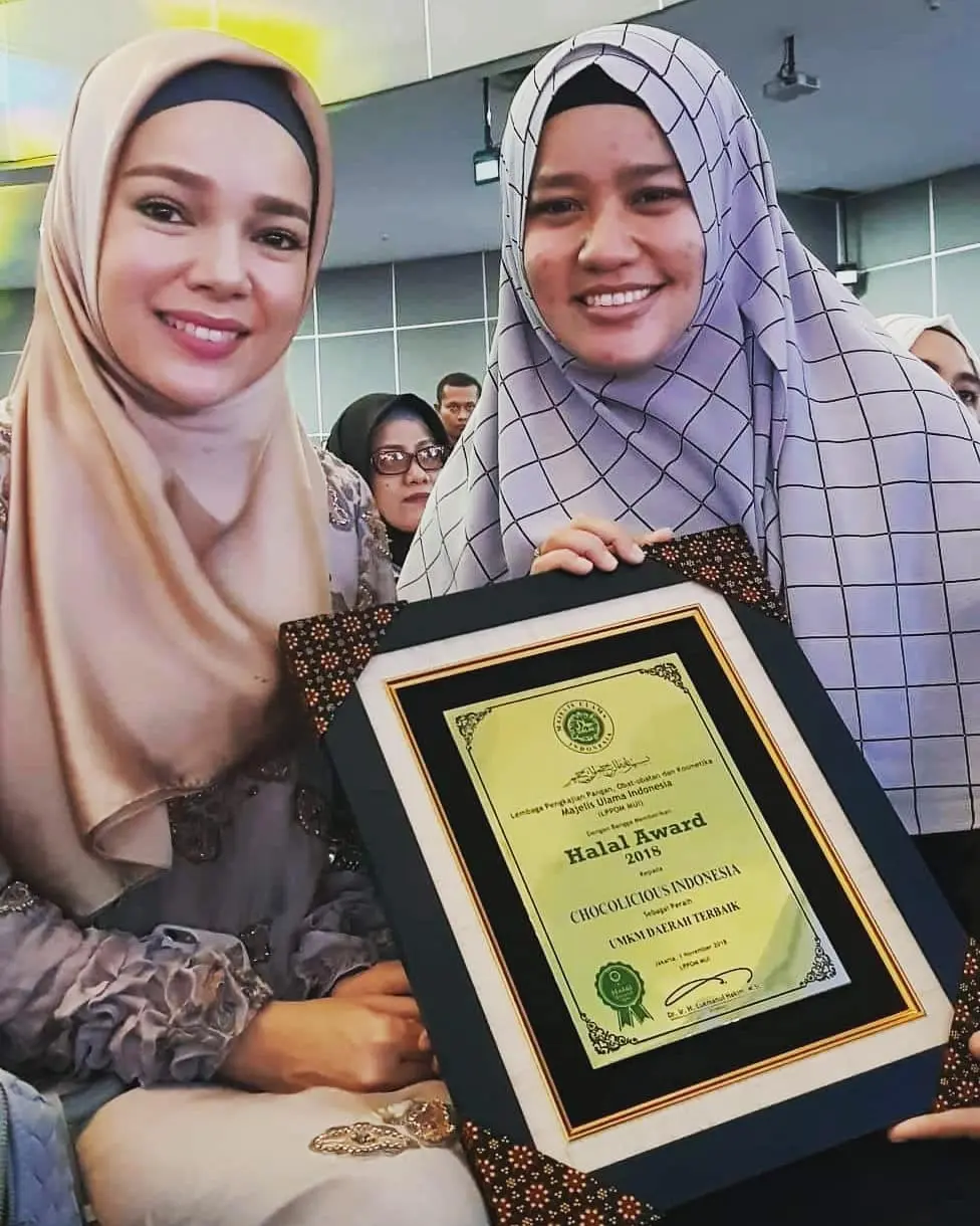 Dewi Sandra tersenyum sambil memegang kue cokelat yang baru dibeli di Toko Cake Chocolicious, menampilkan kebahagiaan dalam kunjungannya